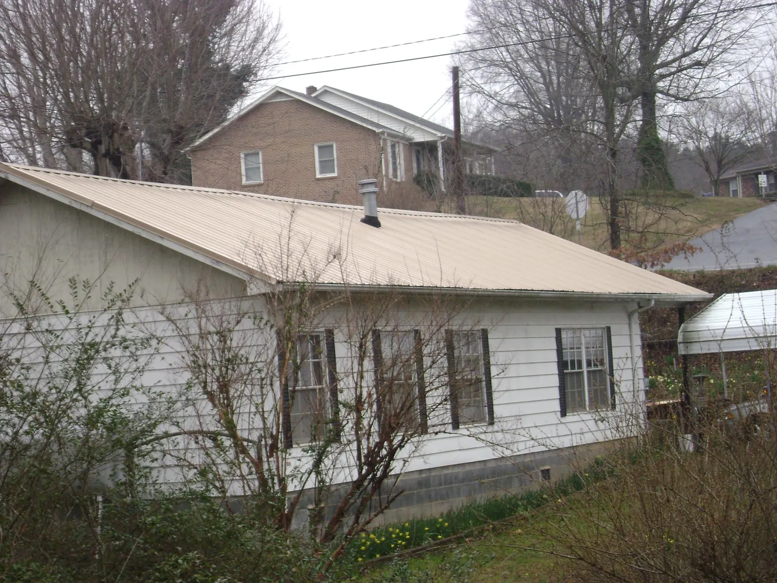 Tan metal roof on a white sided house set into a hillside — Commercial Roofing by Roofing Brothers in Urbana